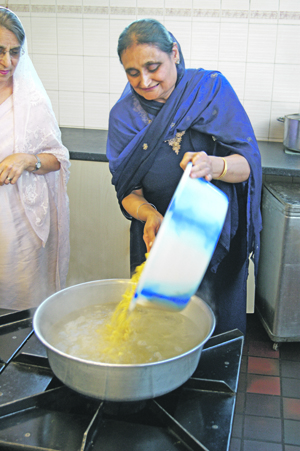 FOOD: A volunteer pours pasta into one of the huge preparation pans as they prepare langar.